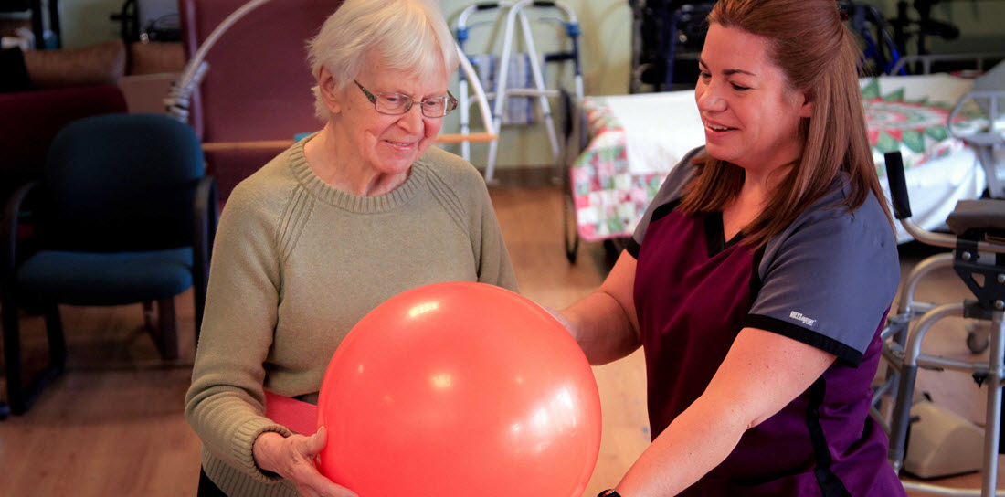 physical therapist helps senior woman with a medicine ball