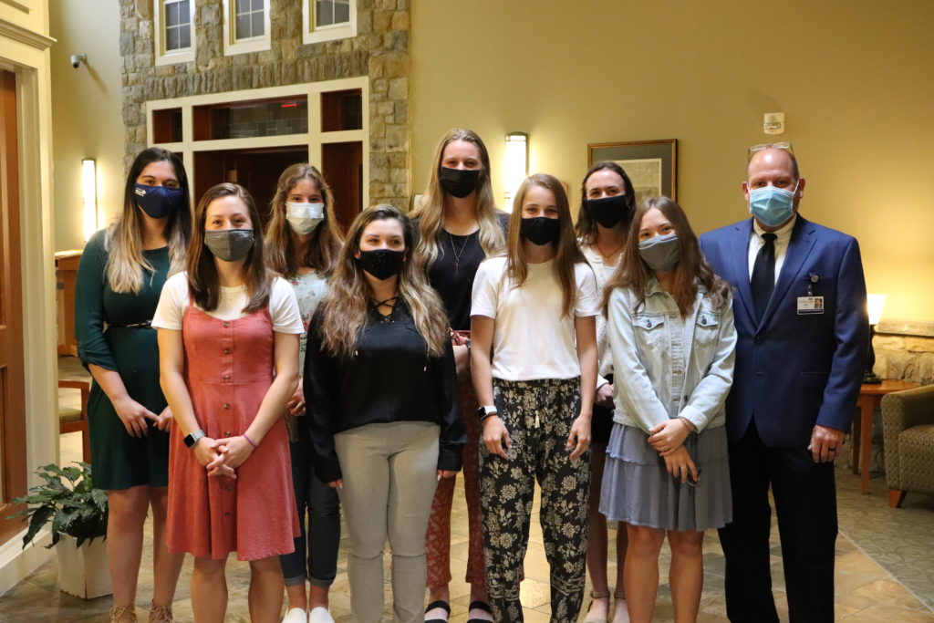 Nine people standing in a hallway with medical face masks.