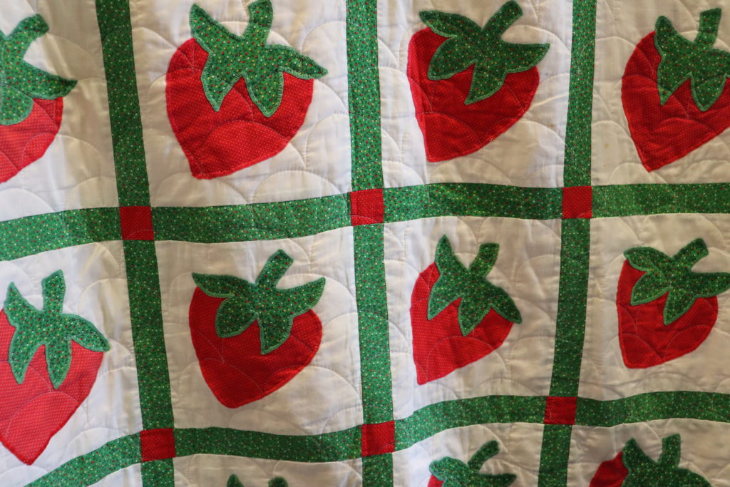 A closeup shot of a handmade quilt with stripes and strawberries.