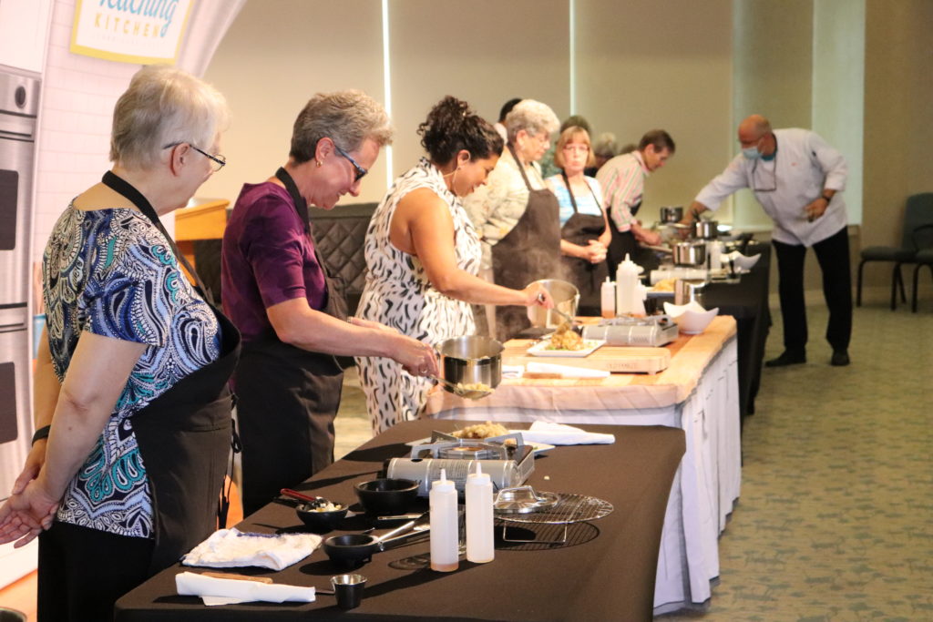 A row of people in front of tables cooking a meal.