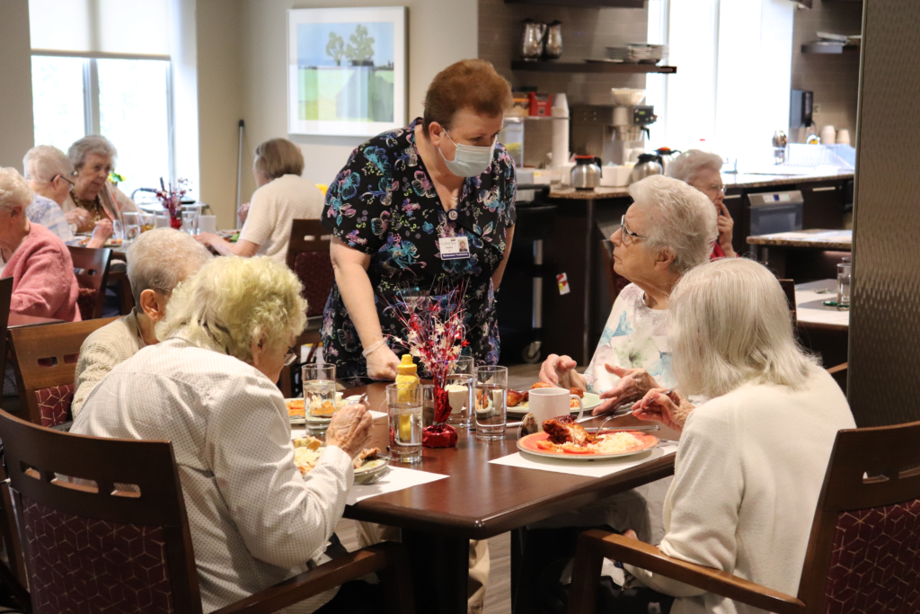 A nurse standing next to a table with four women seated around it.