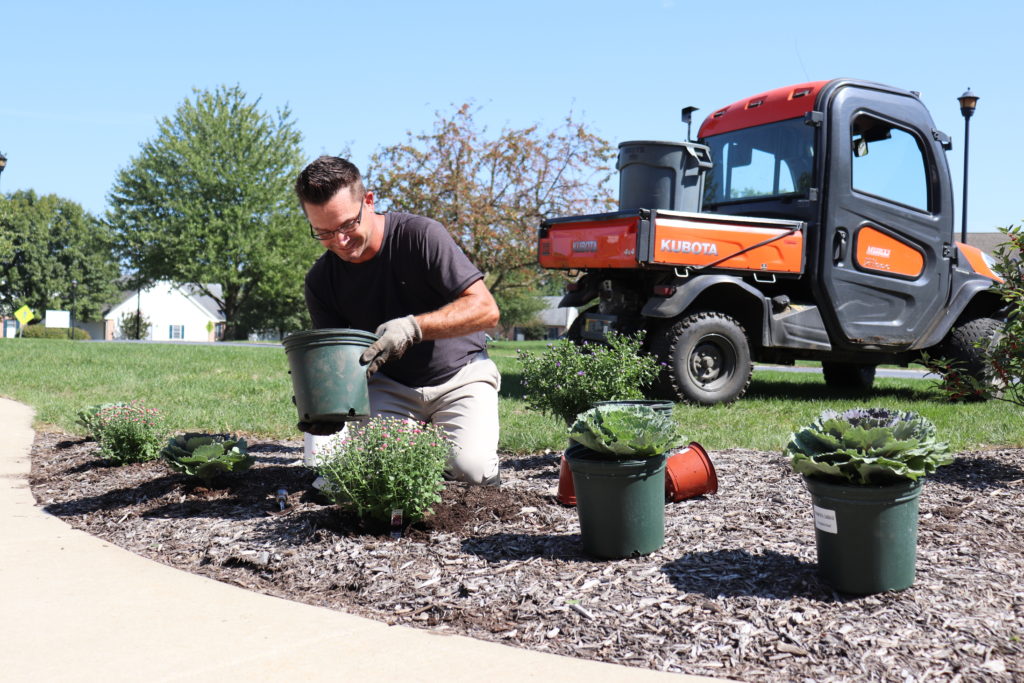 A man kneeling in a flowerbed planting flowers.