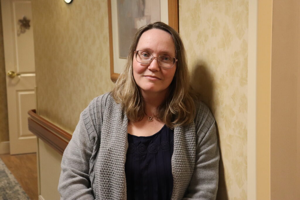 A picture of a woman leaning against a wall in a hallway.