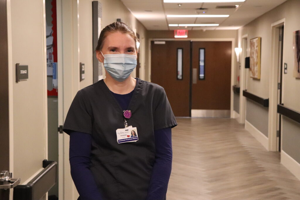 A woman in medical scrubs standing in a hallway of a healthcare facility.