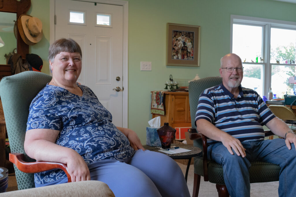 George and Sue Minick smile while they sit in two chairs in the living room of their cottage.