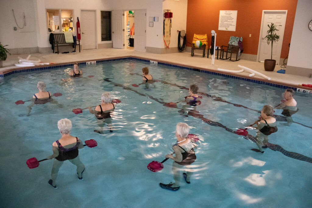 A pool full of people in bathing suits exercising with resistance training bars made for the water. 